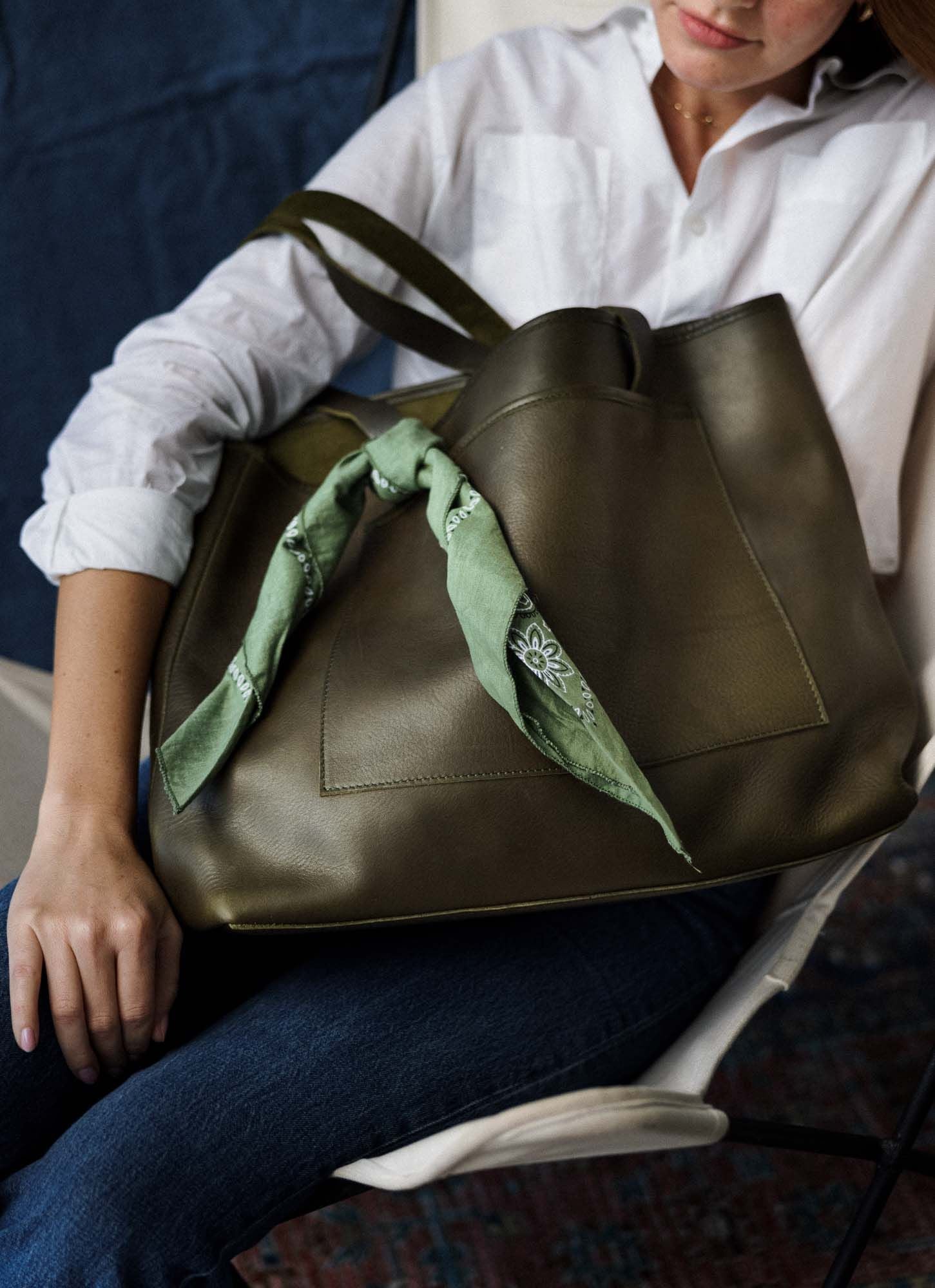 Woman seated with an olive green WP Standard leather tote styled with a green bandana, ideal for casual Mother's Day gifting.