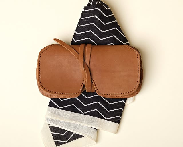 WP Standard brown leather glasses case with tie closure, resting on a black & white patterned handkerchief.