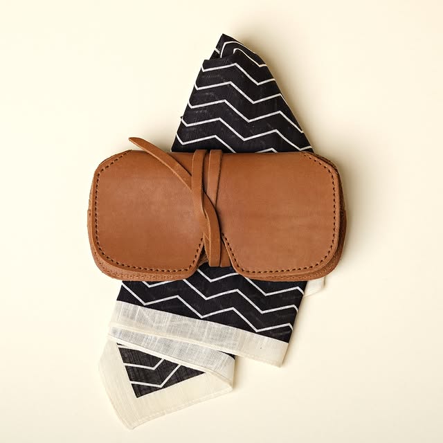 WP Standard brown leather glasses case with tie closure, resting on a black & white patterned handkerchief.