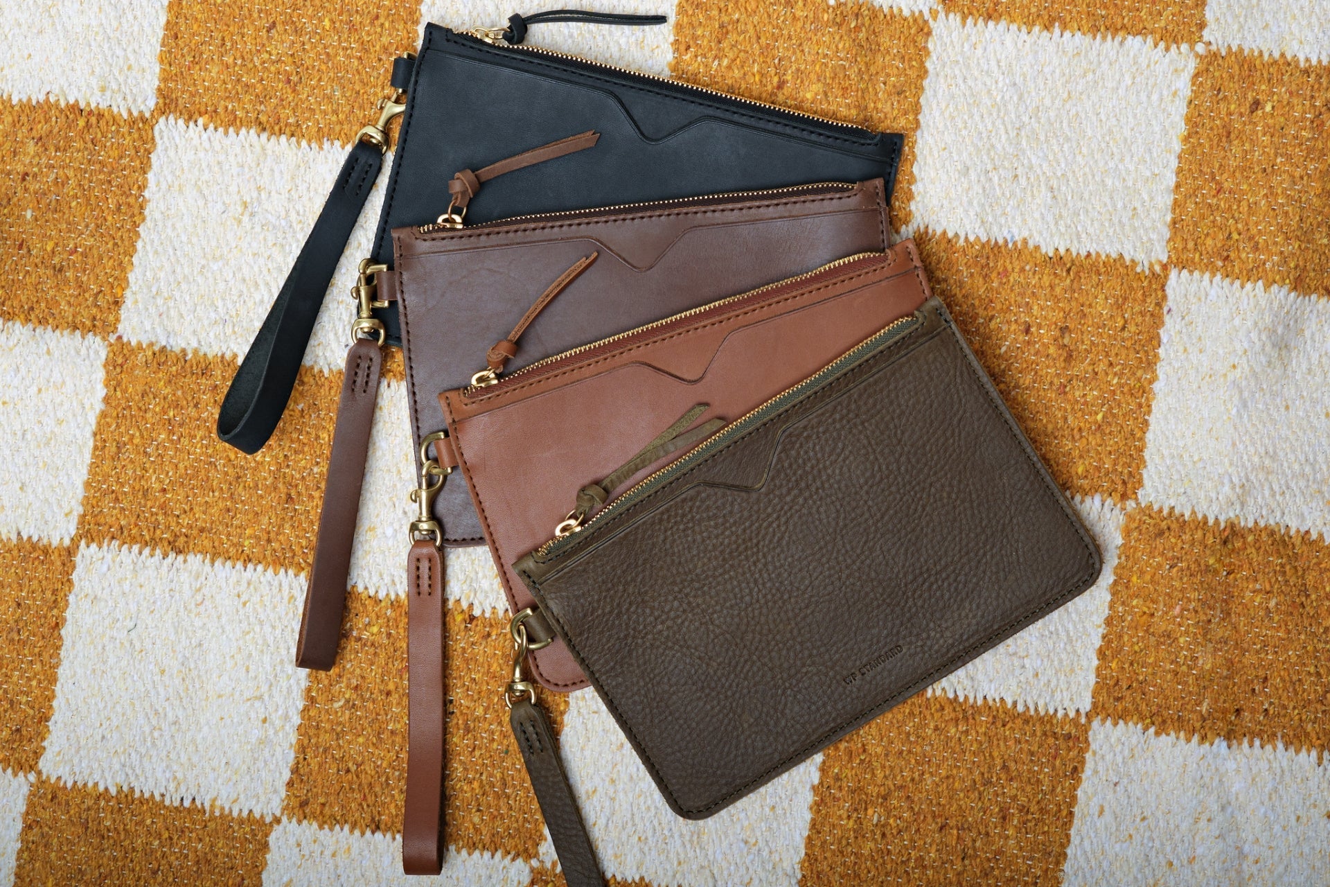 Assorted leather pouches in various colors arranged on a wooden table for minimalist storage.
