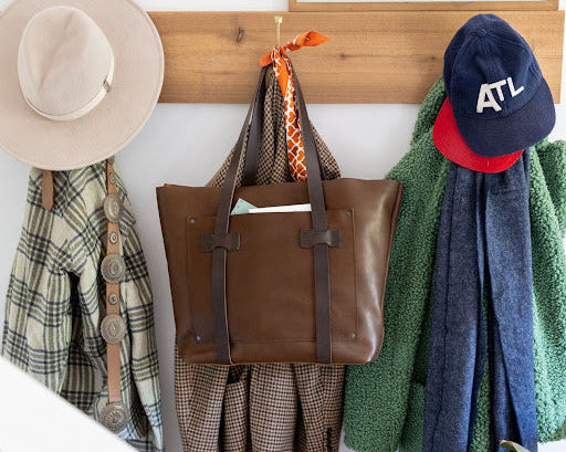 Brown leather tote bag, hanging with a scarf and hat, showcasing timeless fashion.