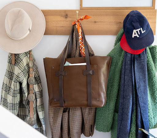 Brown leather tote bag, hanging with a scarf and hat, showcasing timeless fashion.