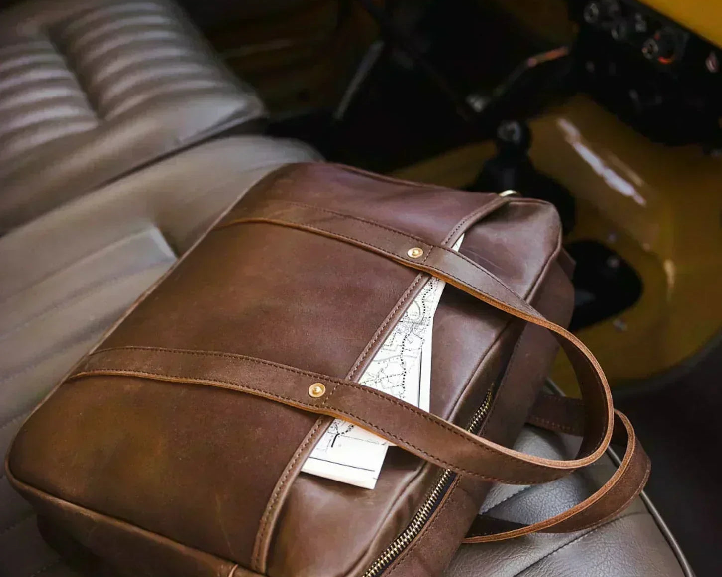 A brown leather Woodward briefcase from WP Standard resting on the passenger seat of a vintage car.