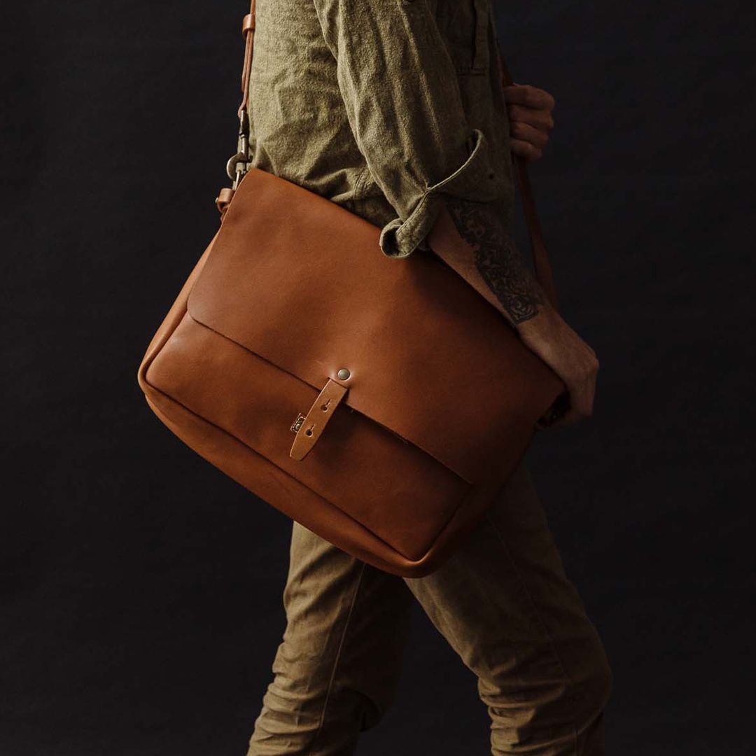 Model wearing a tan full-grain leather messenger bag from WP Standard, styled with olive green shirt and earth-tone pants.