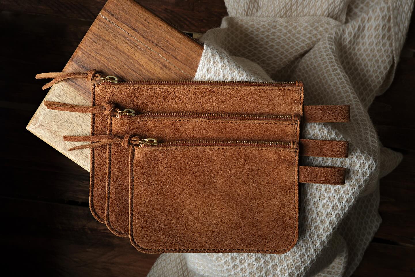 A set of three travel pouches from WP Standard placed on a wooden surface and white cloth on it.. 
