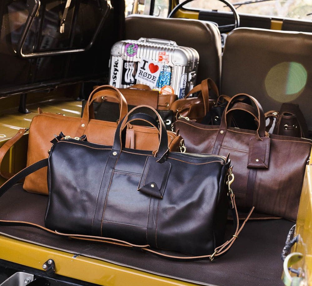 Vibrant weekender bags in assorted colors lined up on a bus doorstep, ready for stylish weekend travel.