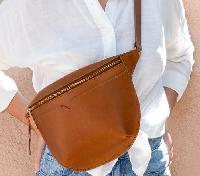 Brown leather crossbody bag worn by a person with a white blouse and denim jeans.