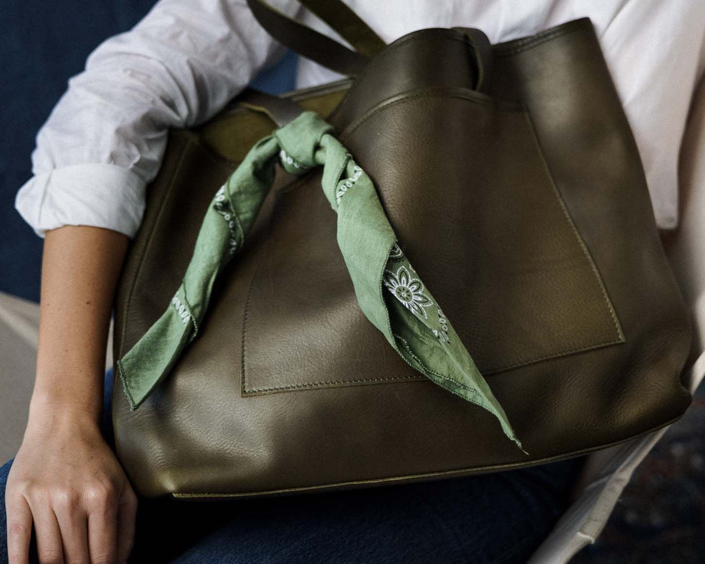 Woman seated with an olive green WP Standard leather tote styled with a green bandana, ideal for casual Mother's Day gifting.