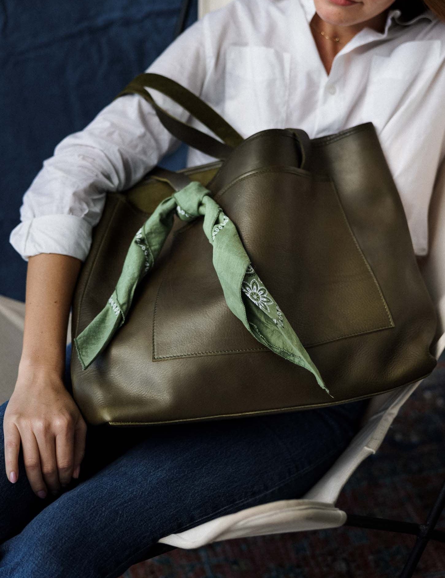 Woman seated with an olive green WP Standard leather tote styled with a green bandana, ideal for casual Mother's Day gifting.