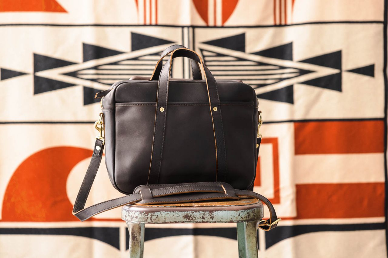 WP Standards’ woodward briefcase on a stool, against a colorful, patterned fabric backdrop.