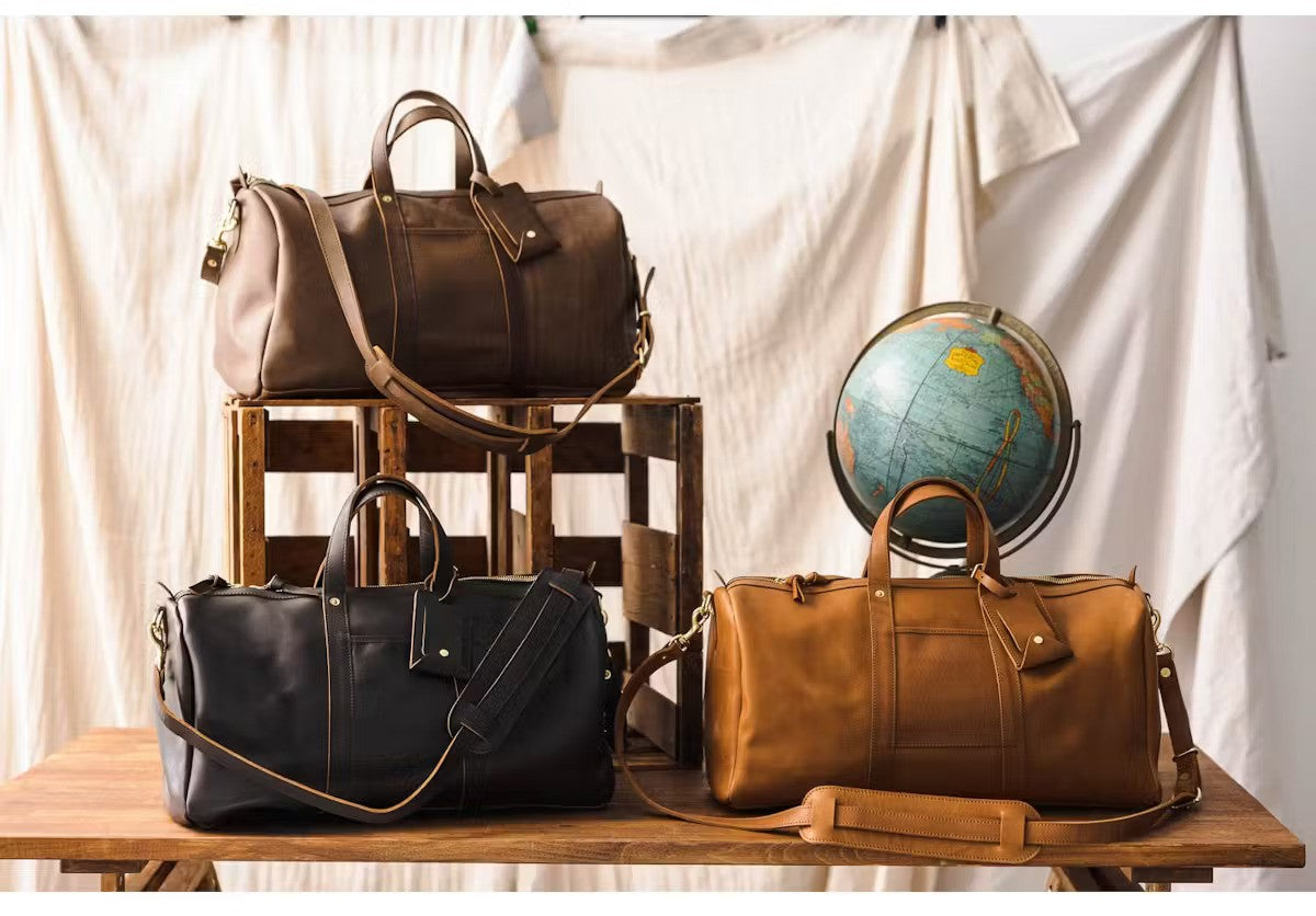 Three leather duffle bags from WP Standard are placed on a wooden table along with a globe.