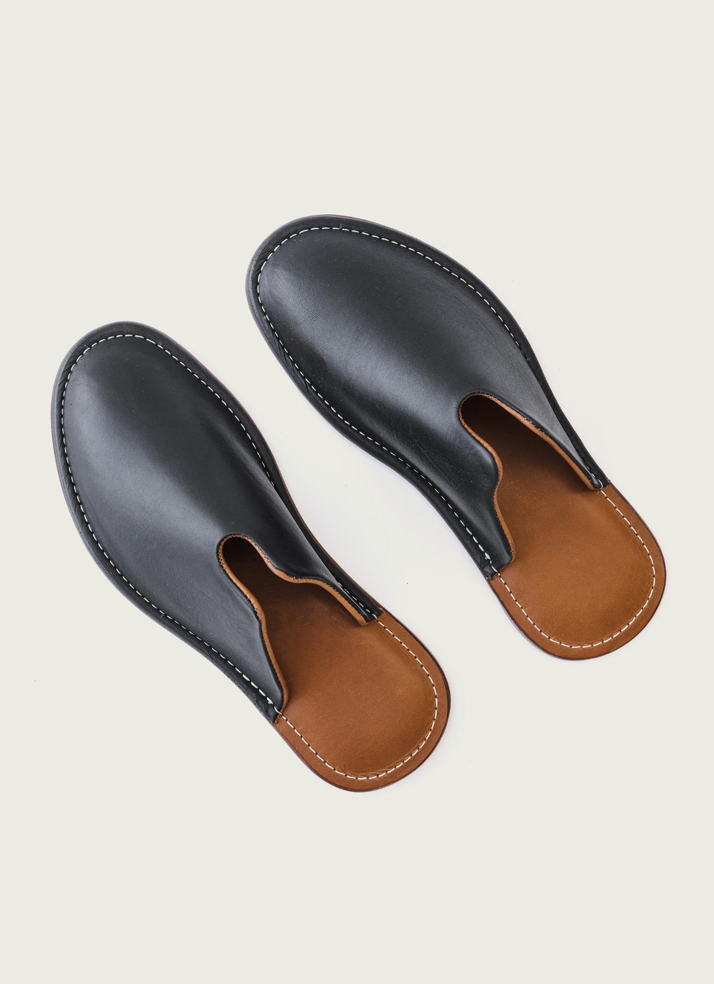 Handcrafted black leather slip-on slippers with brown sole and white stitching – premium quality minimalist footwear for comfort and style.