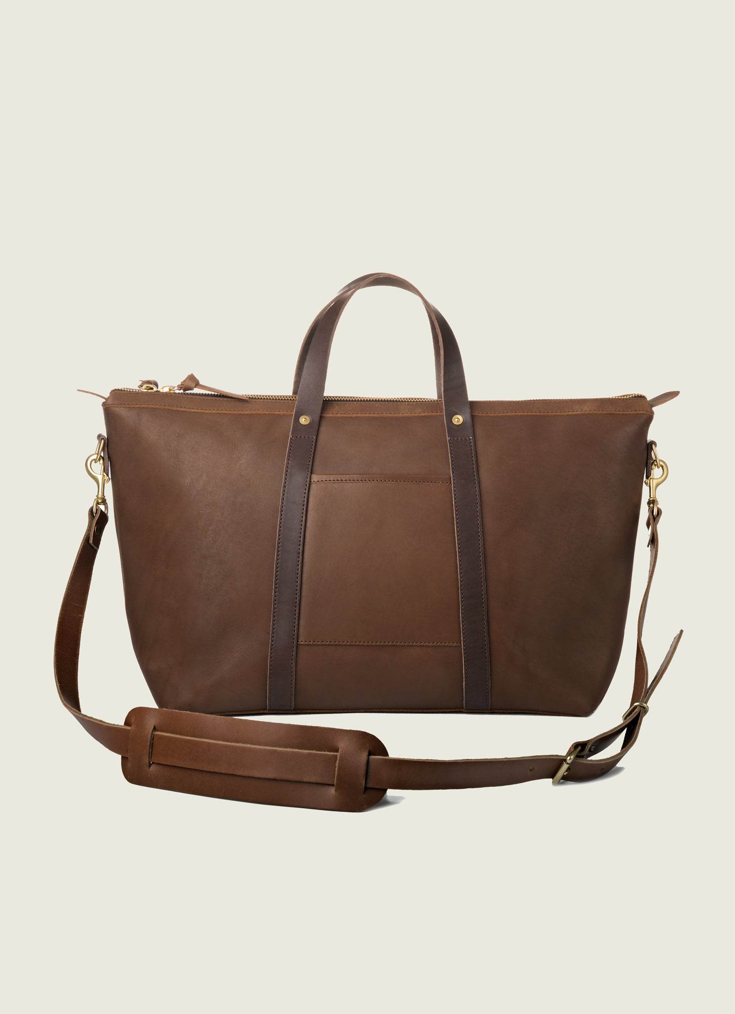 Chocolate brown leather travel tote featuring adjustable strap and solid brass hardware, perfect for stylish commuting.
