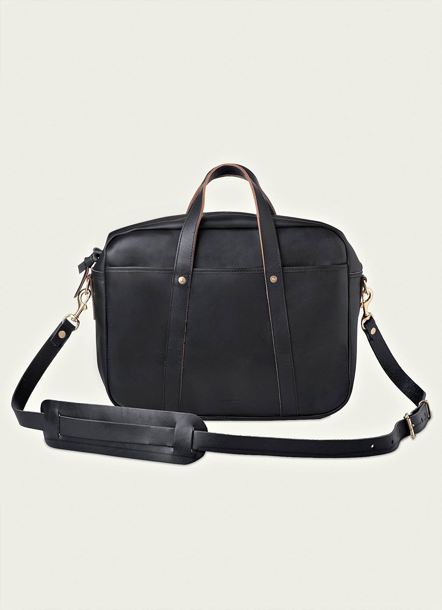 A black full-grain leather briefcase with dual handles, a detachable shoulder strap, and brass hardware, designed for work, travel, and everyday carry.