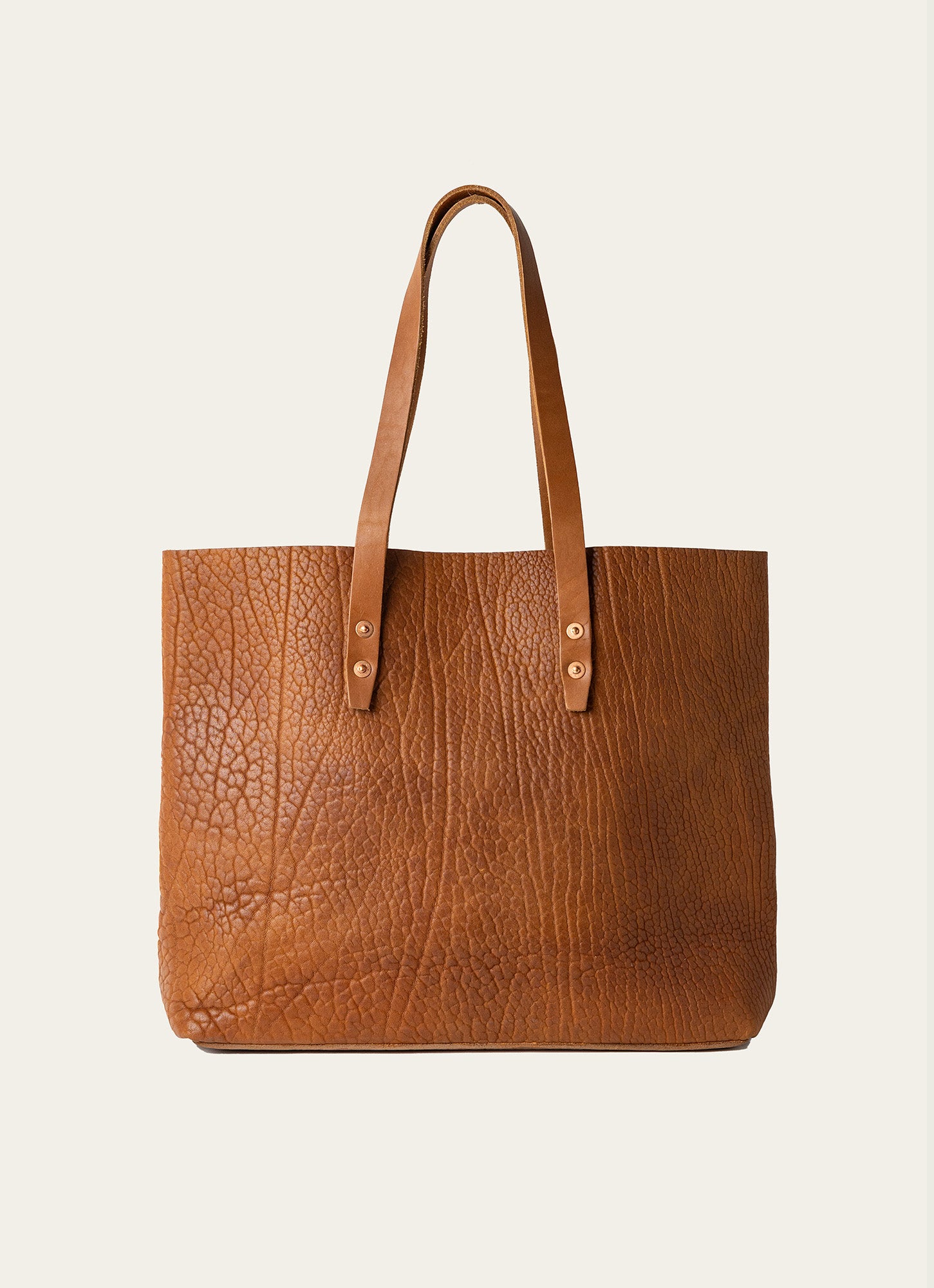 A tan leather tote bag with a textured finish and brass rivet details for added style.