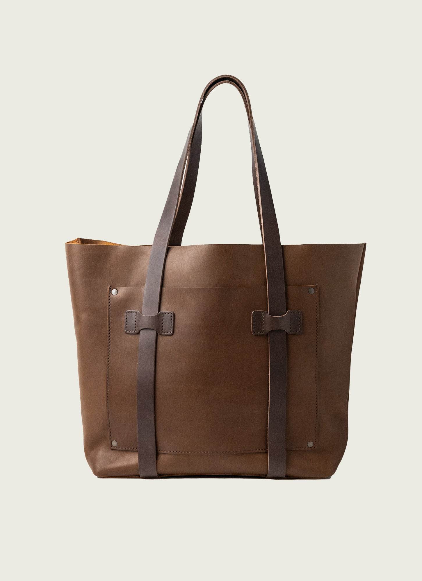 Brown leather tote with dark vertical straps and exposed rivets, crafted for rugged durability and timeless appeal.