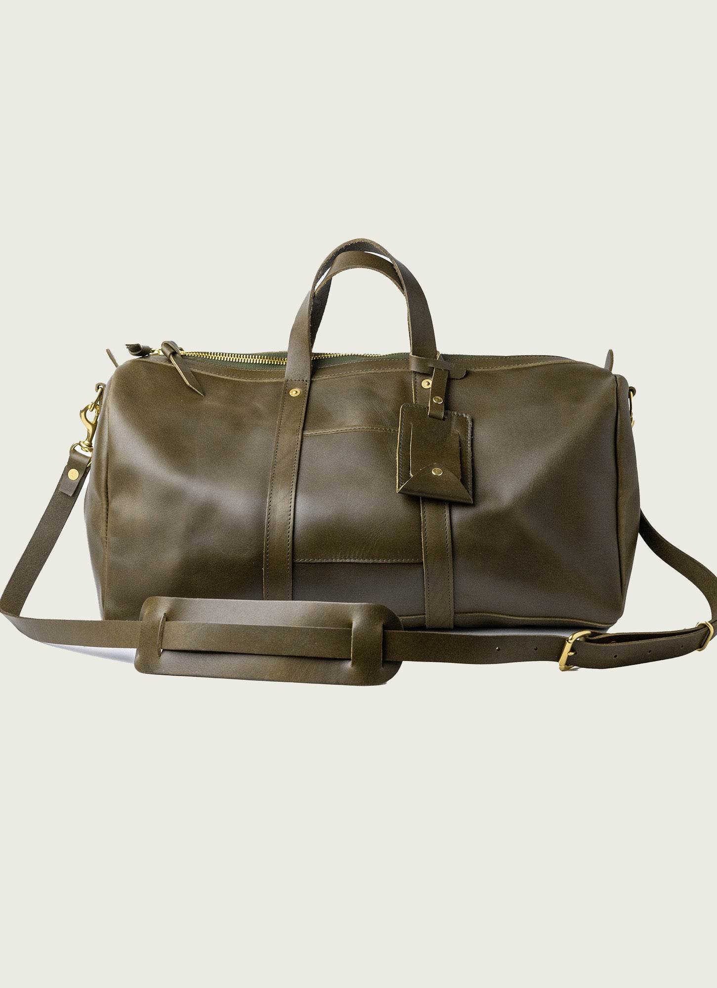 Premium olive green leather duffle bag with adjustable shoulder strap, brass hardware, and luggage tag – perfect for travel, work, or weekend getaways.